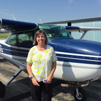 A woman in a yellow shirt is standing in front of a small plane