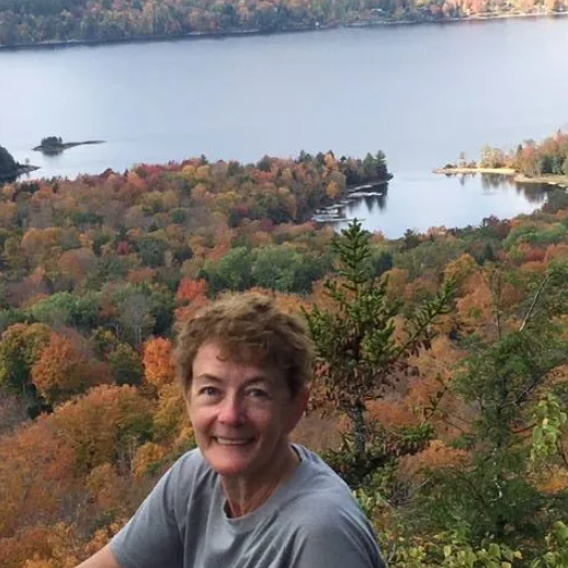 Man in cockpit of plane smiles, adjusting controls; wearing plaid shirt and jeans.