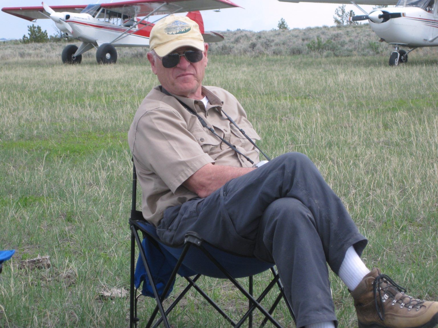 A man sits in a chair in a field with a plane in the background