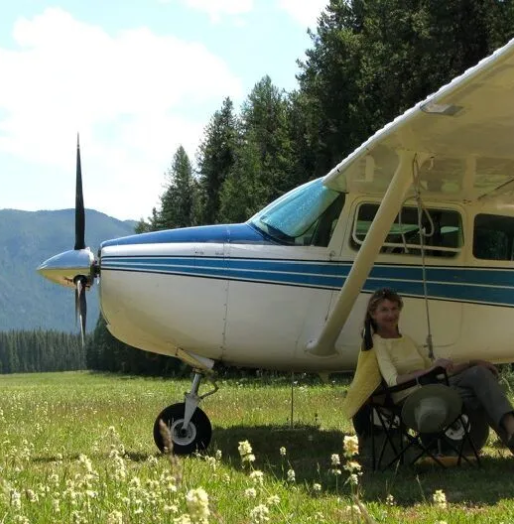 Man in hat and sunglasses in front of a small white airplane on a white plane. Blue sky.
