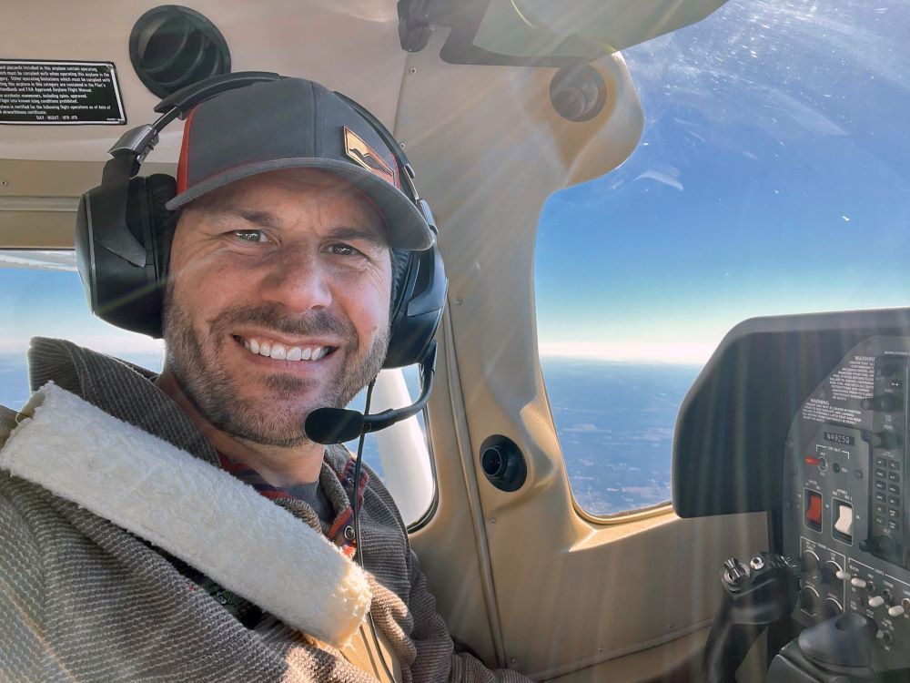 A man wearing headphones and a hat is sitting in the cockpit of an airplane.