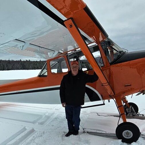 Man standing by an orange and white plane on a snowy runway.
