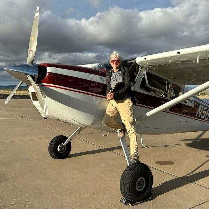 Woman poses on the step of a maroon and white plane at an airfield.