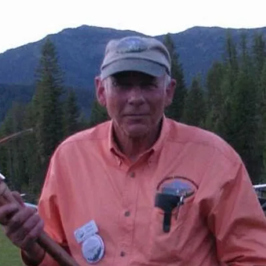 Man in front of brown and red airplane. Smiling with hands on hips. Airport setting.