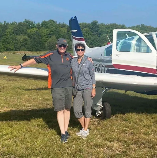 Woman in airplane, smiling with dog, looking out the window.