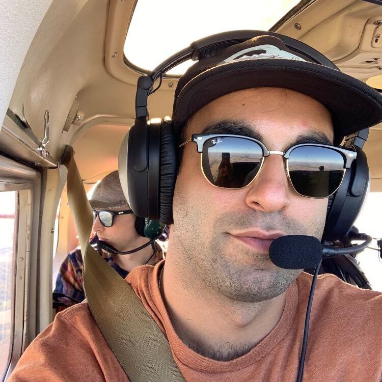 Man in sunglasses and headset, flying a small airplane.