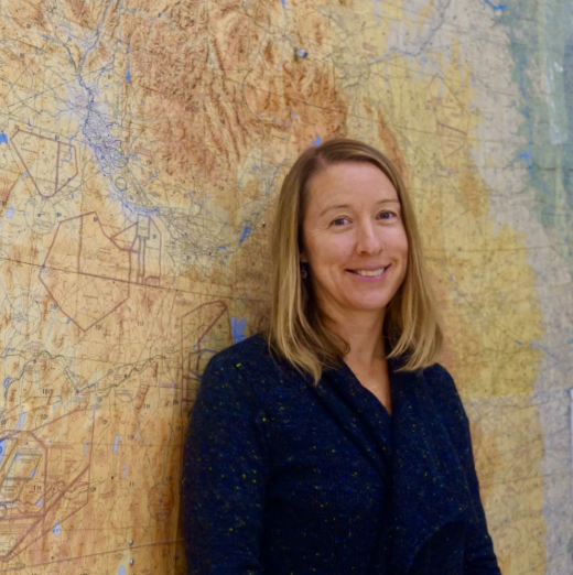 A person standing next to a small plane with mountains in the background
