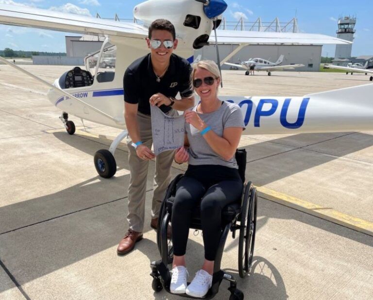 A man stands next to a woman in a wheelchair in front of a plane that says pu
