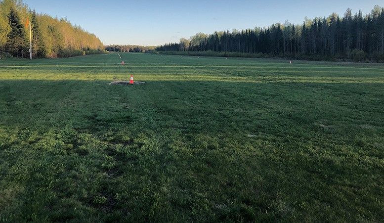 A drone is flying over a grassy field with trees in the background.