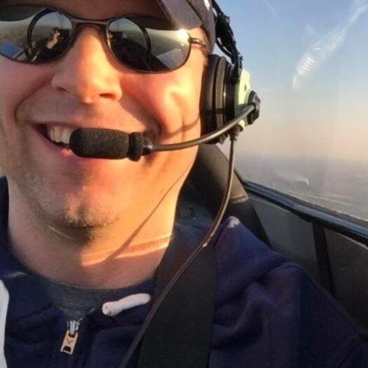 Man wearing sunglasses and headset smiles in an airplane cockpit.