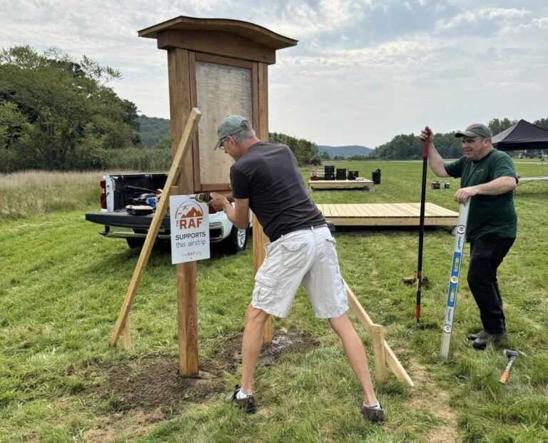 Two men are working on a sign in a field.