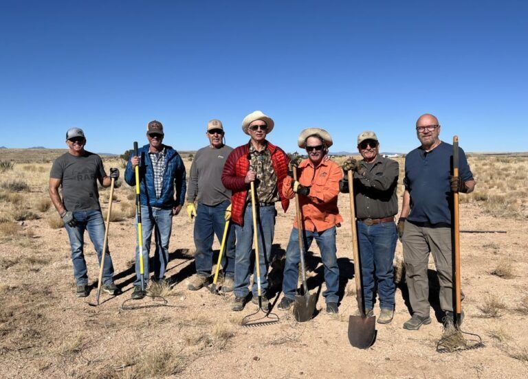 A group of men are standing in a field holding shovels.