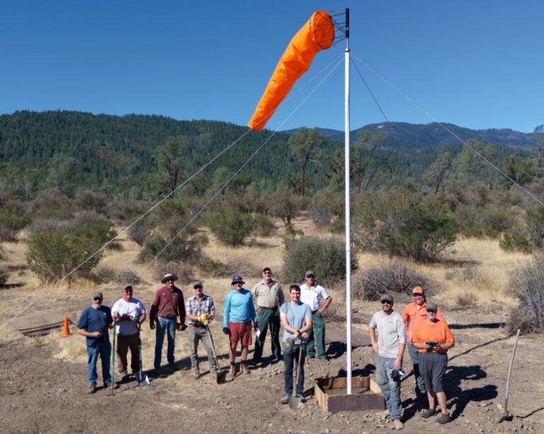 A group of men standing in front of an orange wind cone