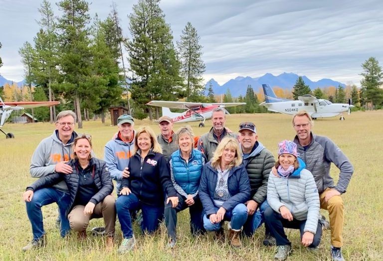 A group of people are posing for a picture in a field with a plane in the background.