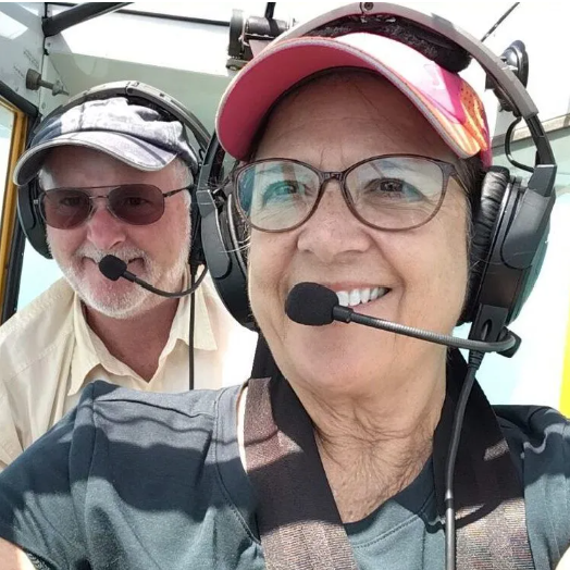 A man in a plaid shirt stands in front of an orange airplane