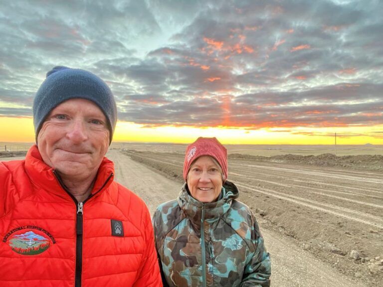 A man and a woman are standing on a dirt road at sunset.