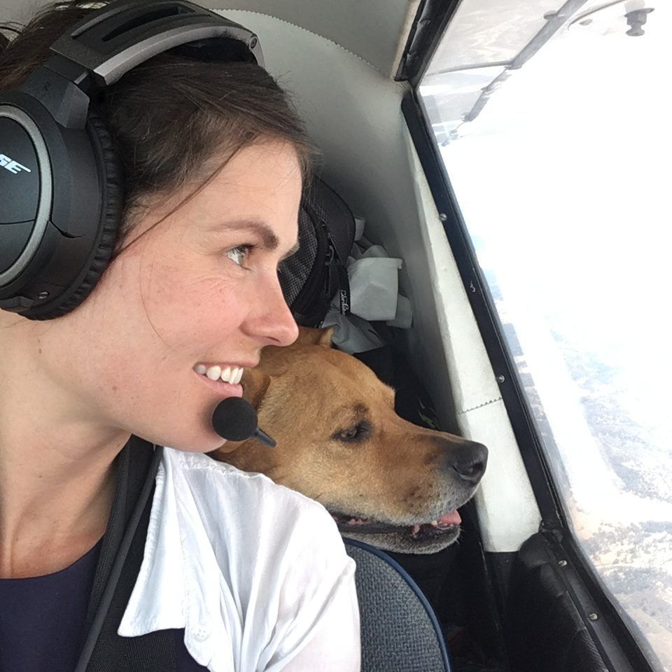 Woman in airplane, smiling with dog, looking out the window.
