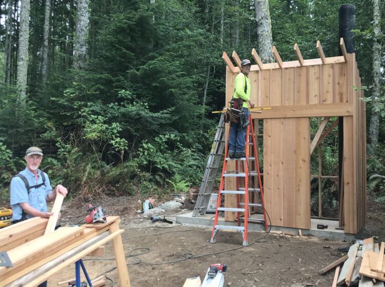 Two men are working on a wooden structure in the woods.