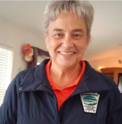 A person standing next to a small plane with mountains in the background