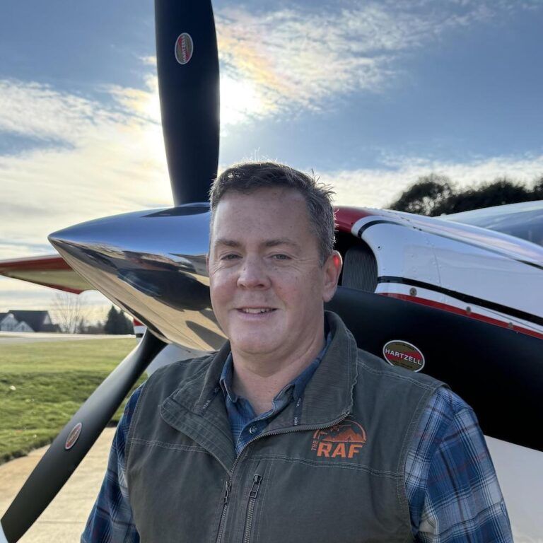 A man wearing a vest that says raf is standing in front of an airplane