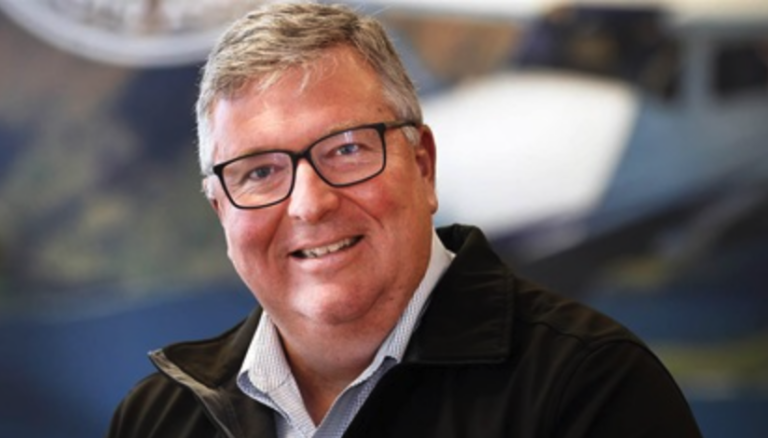A man wearing glasses and a black jacket is smiling for the camera.