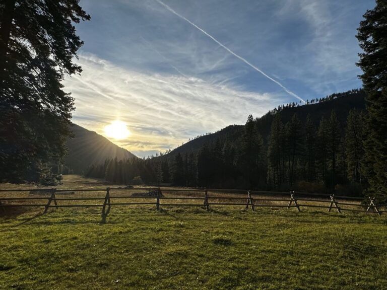 A wooden fence surrounds a grassy field with mountains in the background