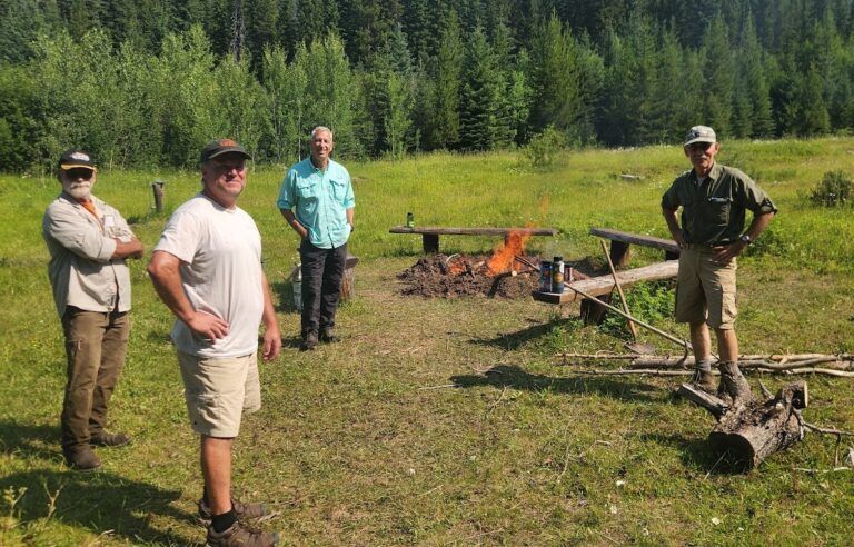A group of men are standing in a field next to a fire pit.