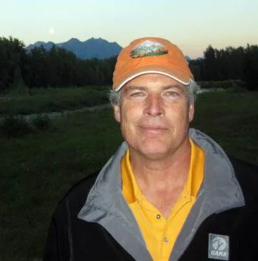 A man in a plaid shirt stands in front of an orange airplane