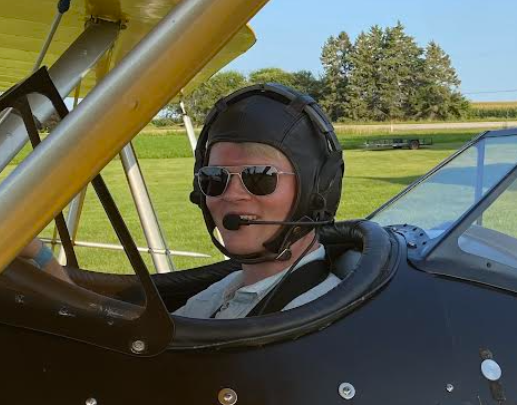 A man wearing a helmet and sunglasses is sitting in a plane