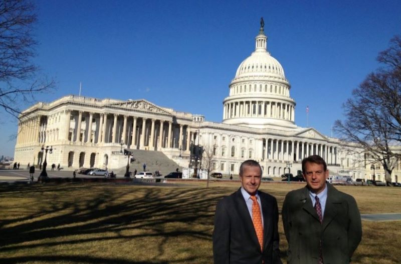 Two men in suits and ties are standing in front of the capitol building.
