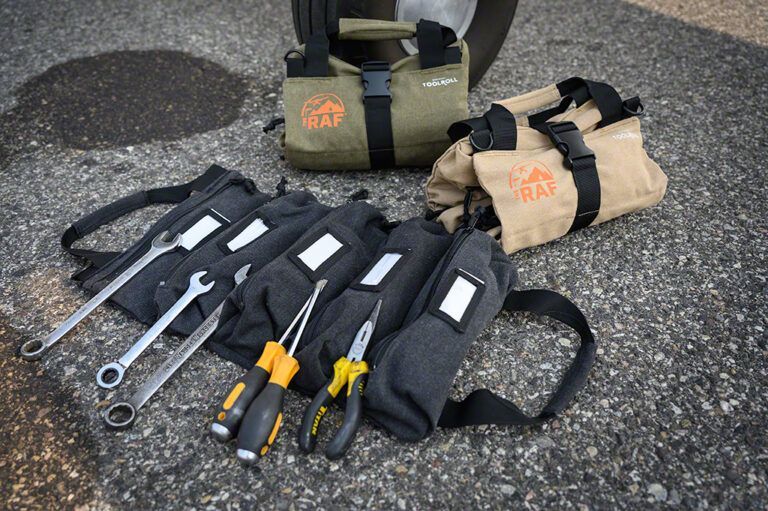 A tool bag filled with tools is sitting on the ground next to a tire.