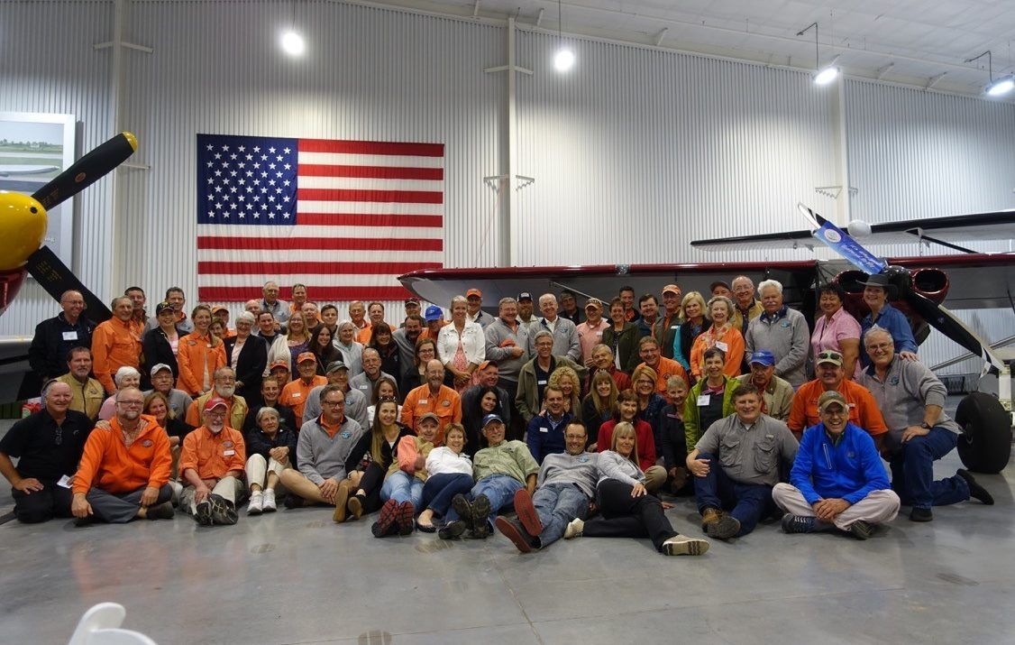 A large group of people are posing for a picture in front of an american flag