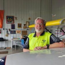 Man in yellow vest sits on plane wing in hangar.