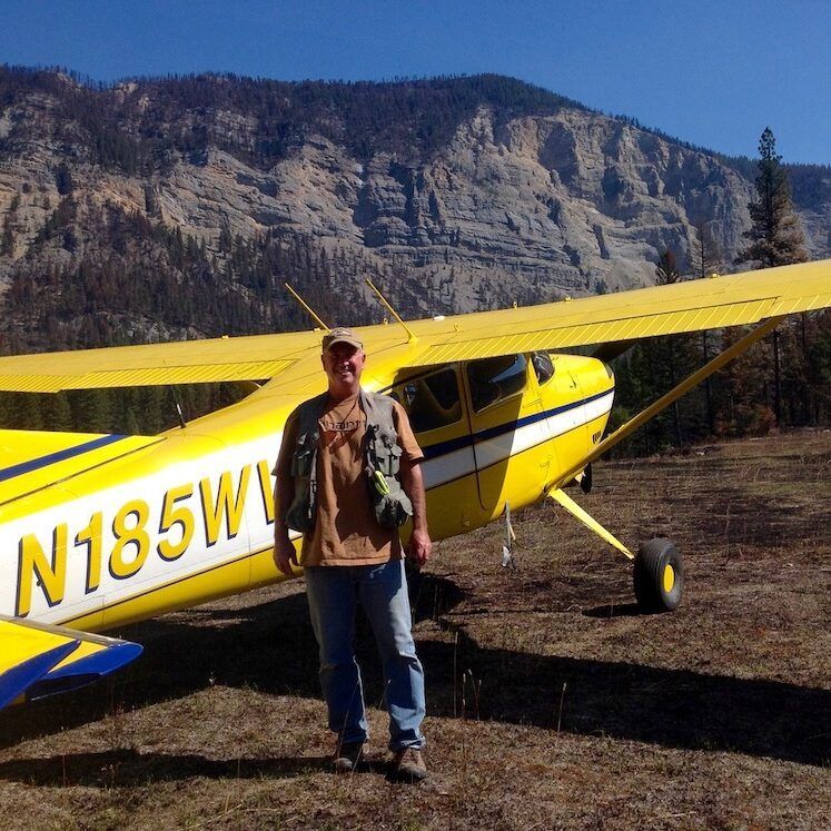Man stands near a yellow airplane in a mountainous landscape.