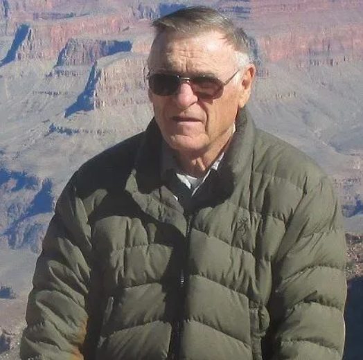 Man in plaid shirt and cap, next to a yellow floatplane, holding its wing.