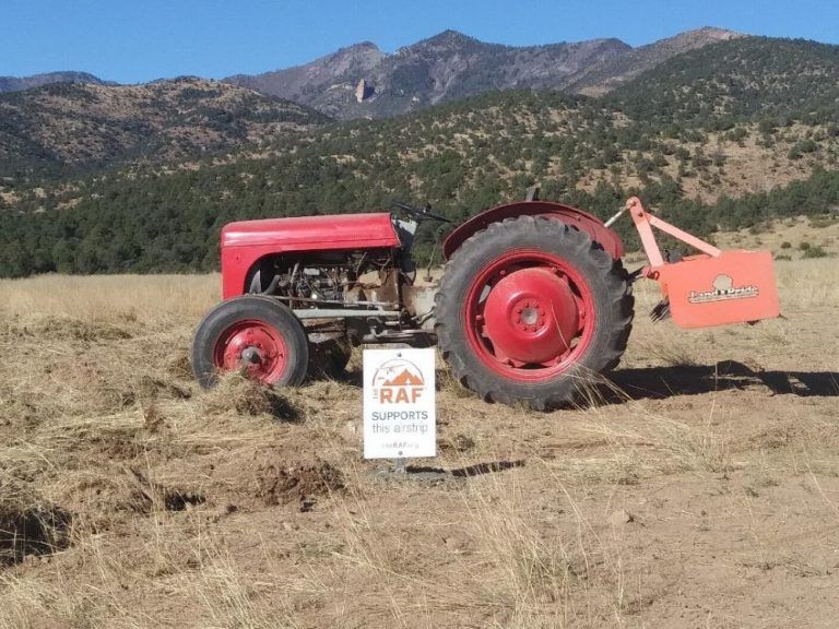 A red tractor is parked in a field with mountains in the background
