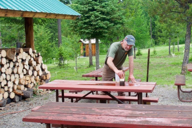 A man is cleaning a picnic table in a park.