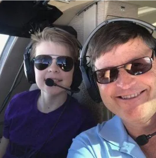 Man in plaid shirt and cap, next to a yellow floatplane, holding its wing.
