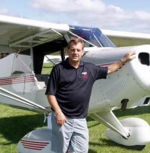 A man wearing a brown leather jacket and a blue shirt is smiling for the camera.