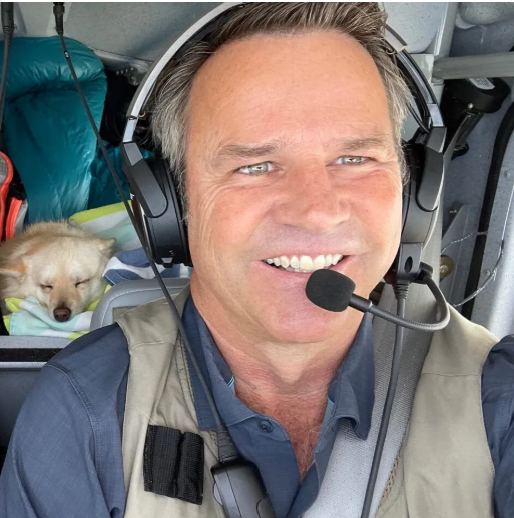 A person standing next to a small plane with mountains in the background