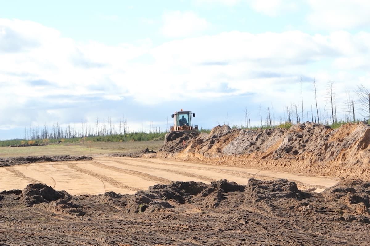 A tractor is plowing a dirt field on a sunny day.