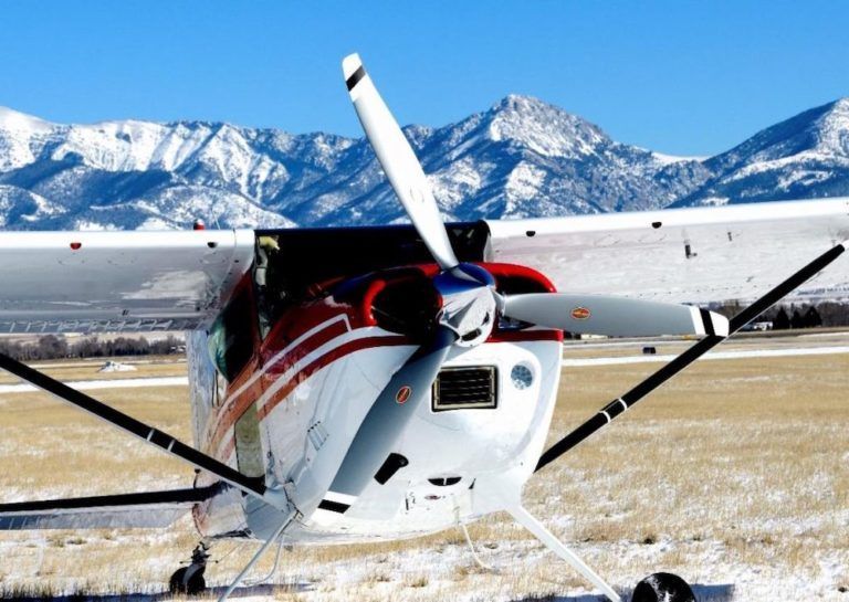 A small plane is parked in a snowy field with mountains in the background