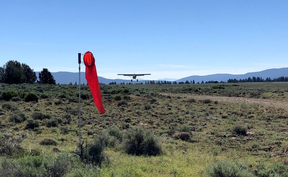 A plane is flying over a field with a red flag in the foreground.