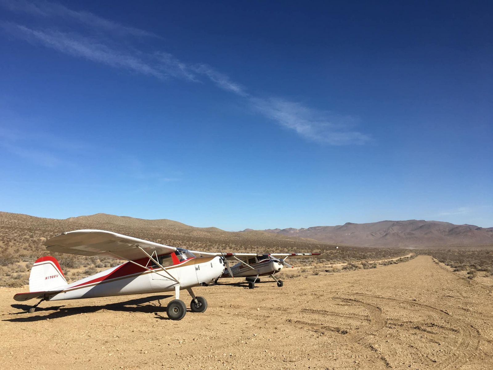 Two small planes are parked on a dirt road in the desert.