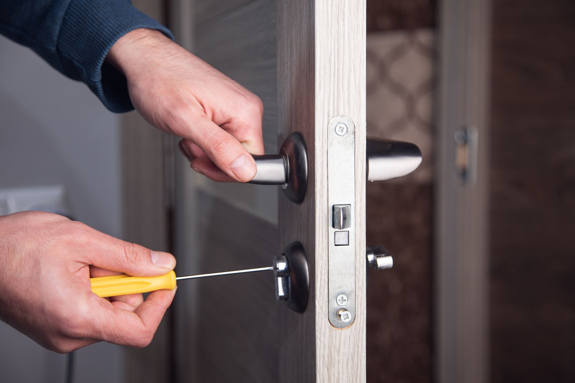 A hand using a screwdriver to install lock hardware on a wooden interior door frame A hand using a screwdriver to install lock hardware on a wooden interior door frame