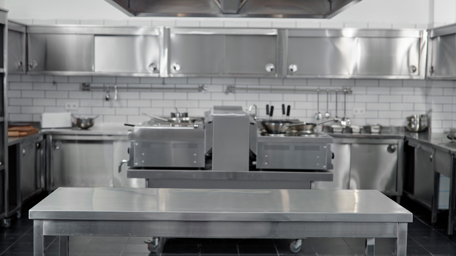Commercial kitchen with stainless steel counters, appliances, and white tile backsplash.