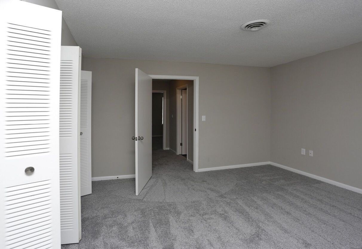 An empty bedroom with a gray carpet and white doors