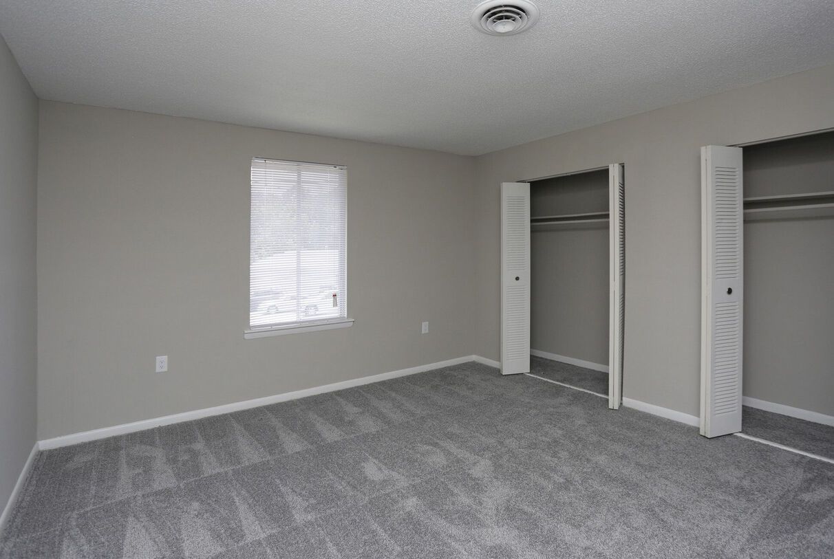 An empty bedroom with two closets and a window.