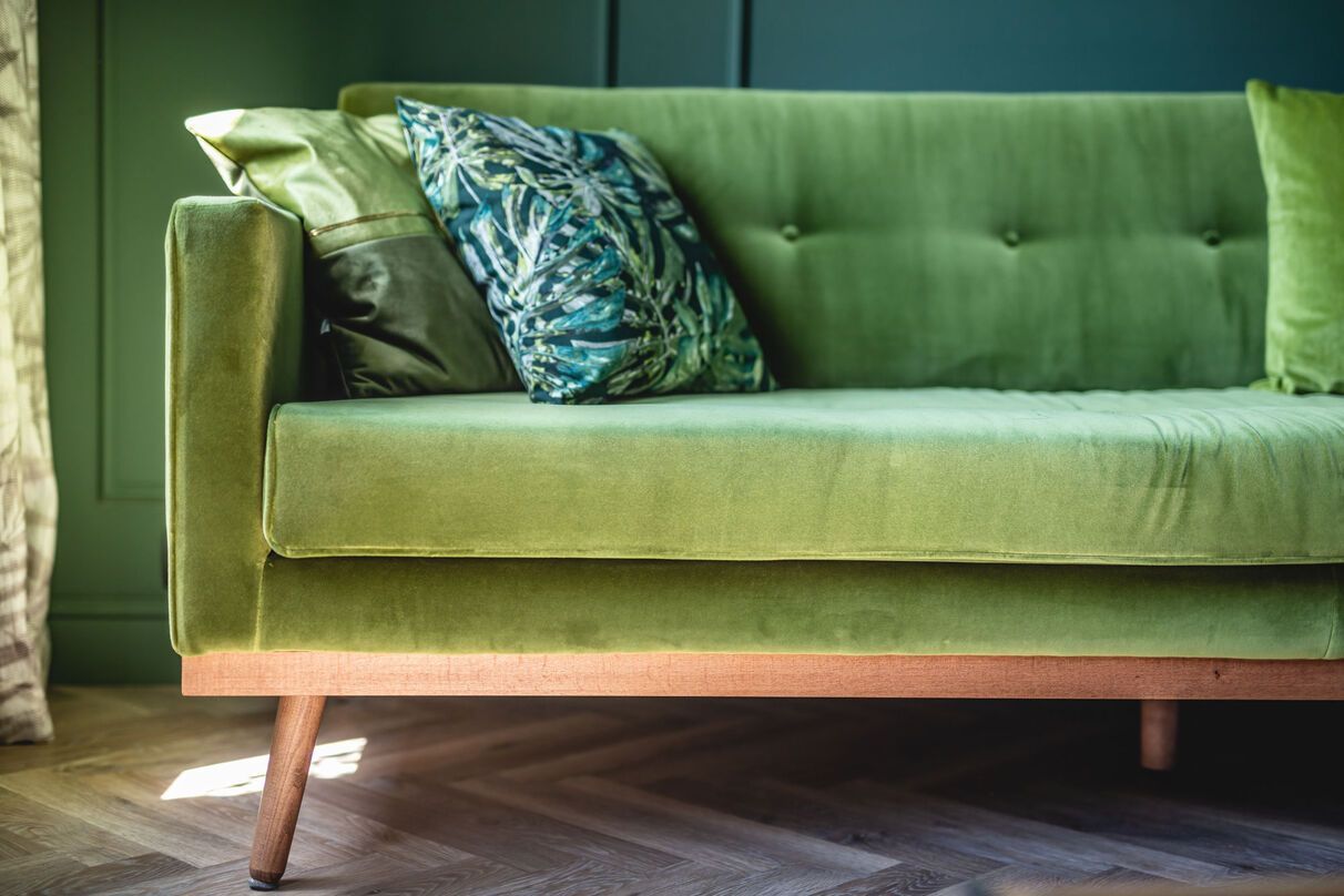 A green couch with pillows on it is sitting on a wooden floor in a living room.