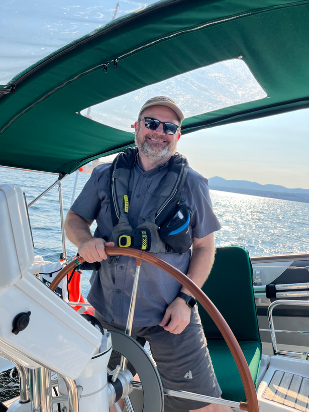 A man is sitting at the steering wheel of a boat.